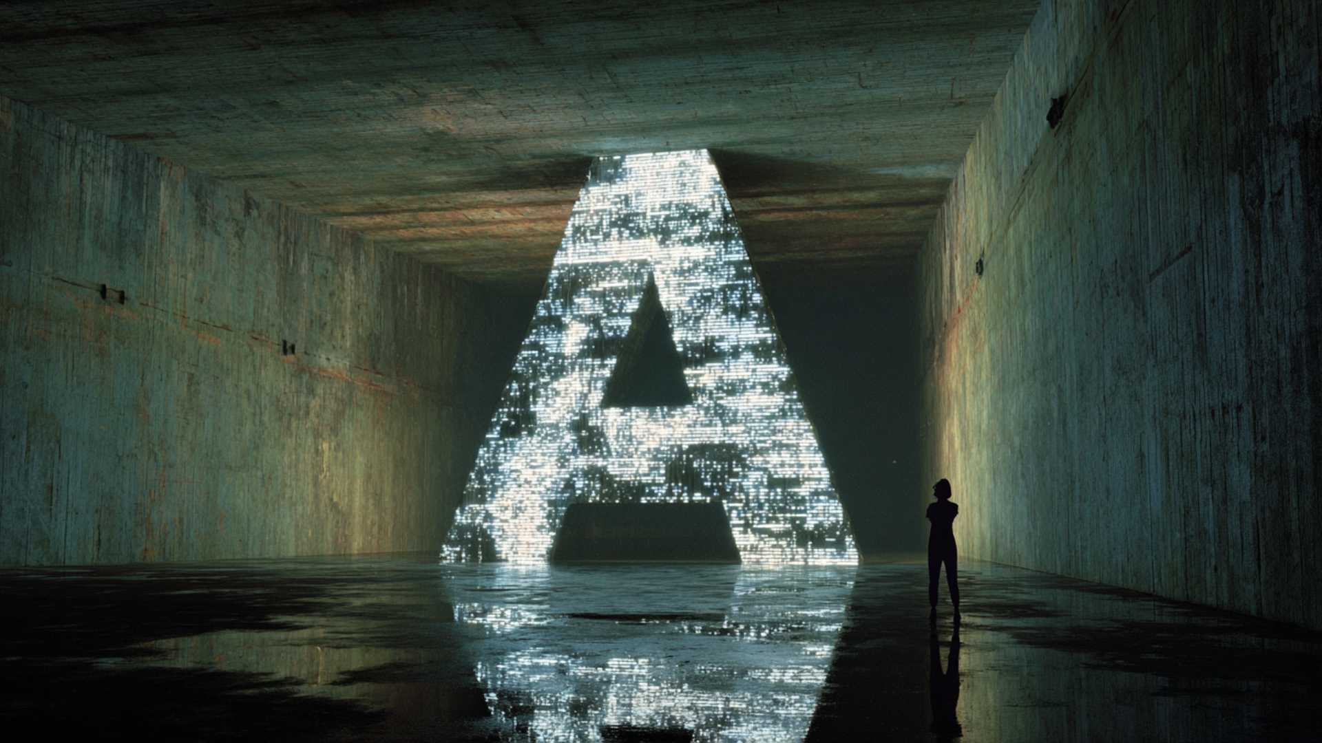 A lone figure stands beside a towering, pixelated letter A in a bare concrete hall.